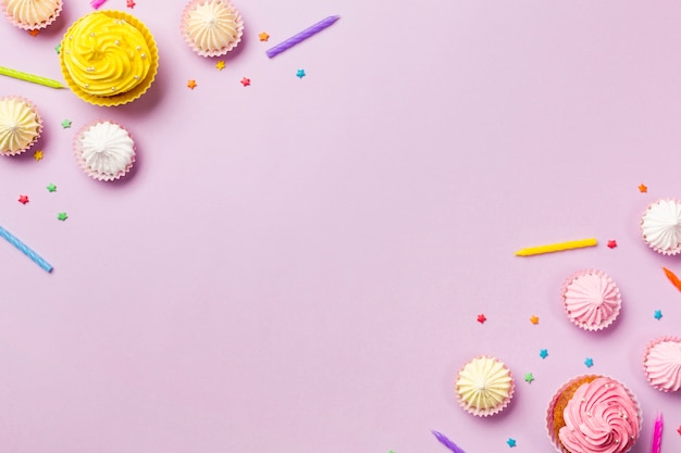 muffins; kaarsen; aalaw en hagelslag op de hoek van roze achtergrond
