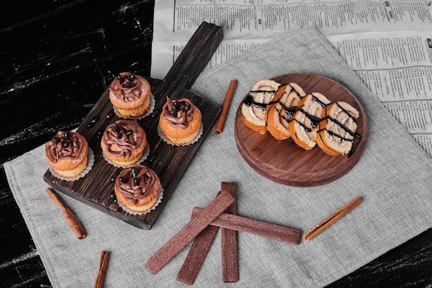 Muffins met cacaoroom op een houten bord met rollcake plakjes.