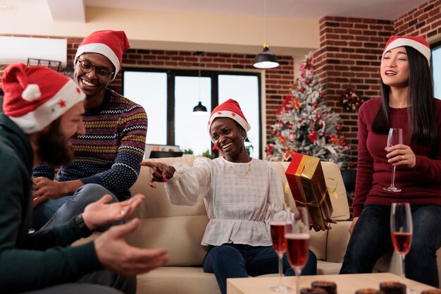 Multi-etnisch team van collega's die geschenken uitwisselen op kerstfeest op kantoor, kerstfeest vieren met alcohol en cadeautjes. Plezier hebben met verrassing bij vakantieviering.
