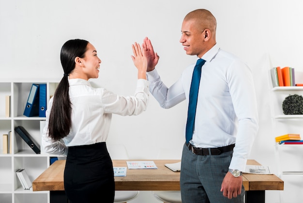 Multi-etnische jonge zakenman en zakenvrouw geven high-five aan elkaar op het werk