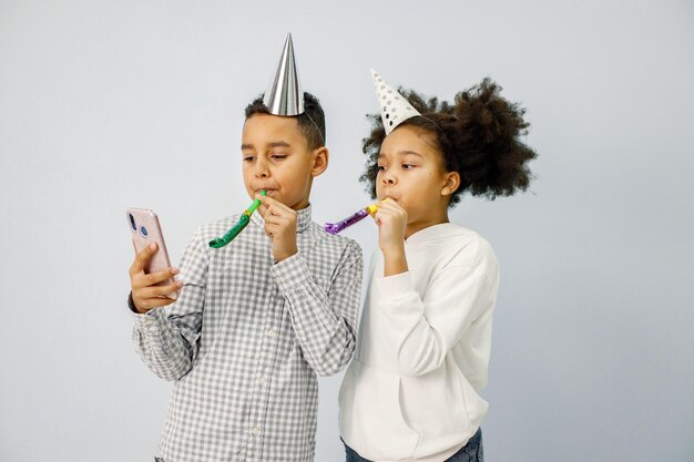 Multiraciale jongen en meisje in verjaardagspet die feesthoorn blaast