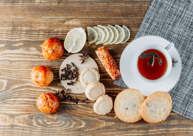 Muntachtige thee in een kopje met gesneden citroen, koekjes, kruidnagel bovenaanzicht op houten tafel