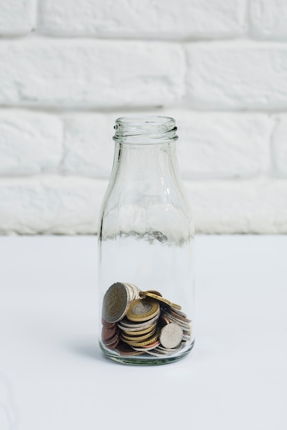 Muntstukken die in de fles van het melkglas tegen witte muur worden verzameld