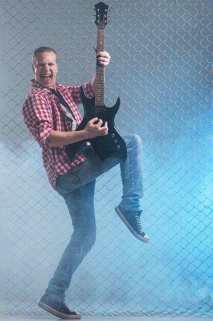 Muziek. Jonge muzikant met een gitaar op hek muur