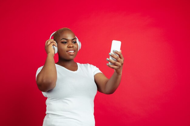 Muziek luisteren, spelen. portret van een afro-amerikaanse jonge vrouw op rood