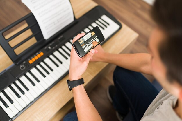 Muziekleraar doet een online videogesprek met een smartphone. Jonge man die keyboard speelt terwijl hij pianolessen op afstand geeft