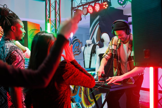 Muzikant die elektronische muziek speelt tijdens live optredens in nachtclub. Dj in koptelefoon mixt geluid op het controllerpaneel op het podium terwijl het publiek feest in de discotheek in de club