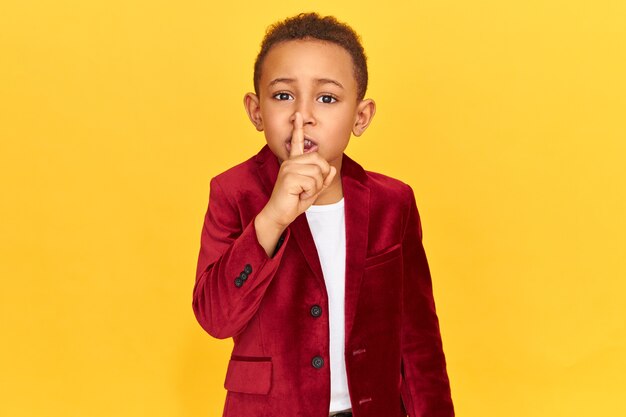 Mysterieuze jongen in stijlvolle kleding zwijgen gebaar maken met wijsvinger op zijn lippen