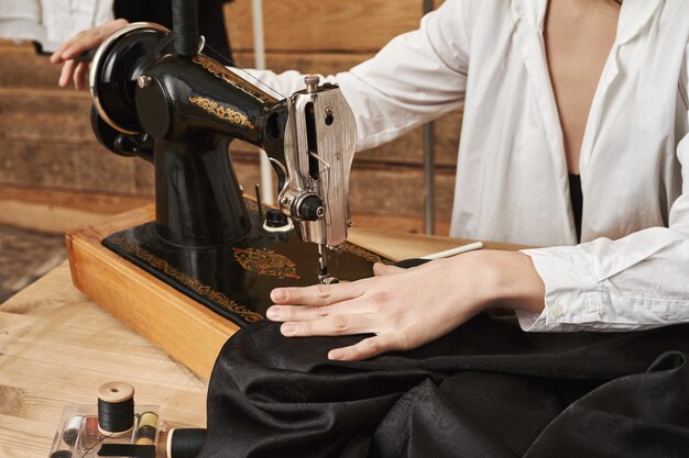 Naaister bezig met nieuw project. Vrouwelijk riool dat met stof werkt, modieus kledingstuk met naaimachine in haar werkplaats creëert, geconcentreerd op naald om naad er netjes uit te laten zien