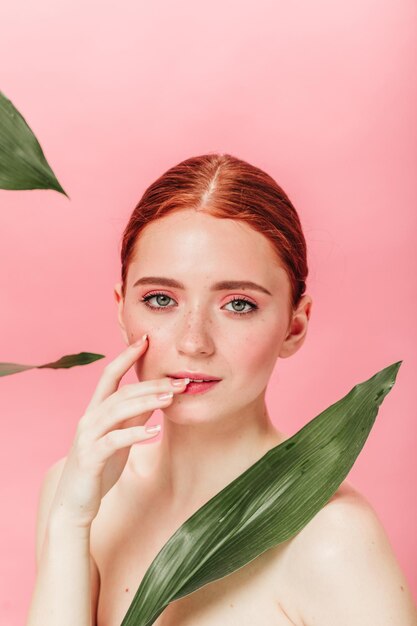 Naakt Kaukasisch meisje met groene bladeren kijken naar camera Studio shot van spectaculaire gember vrouw met plant geïsoleerd op roze achtergrond