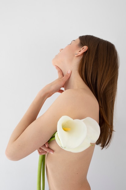 Gratis foto naakte vrouw poseren met bloemen zijaanzicht