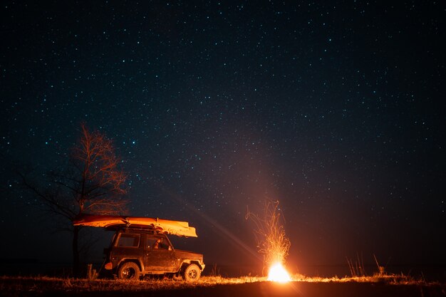 Nachtlandschap met helder kampvuur en auto