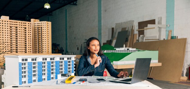 Nadenkend Afrikaans-Amerikaanse dame met laptop en model van gebouw