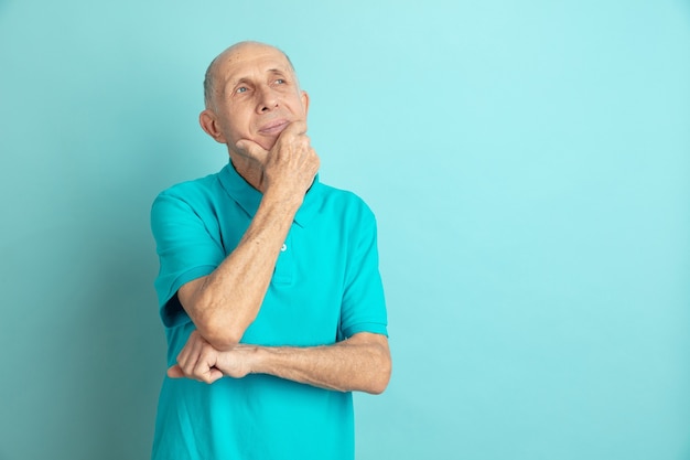 Nadenkend, dromend. Portret Kaukasische senior man geïsoleerd op blauwe studio achtergrond. Mooi mannelijk emotioneel model. Concept van menselijke emoties, gezichtsuitdrukking, verkoop, welzijn, advertentie. Copyspace.