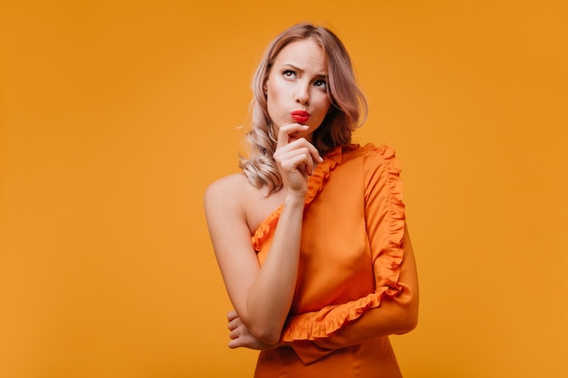 Nadenkend krullende vrouw die in oranje kleding omhoog kijkt