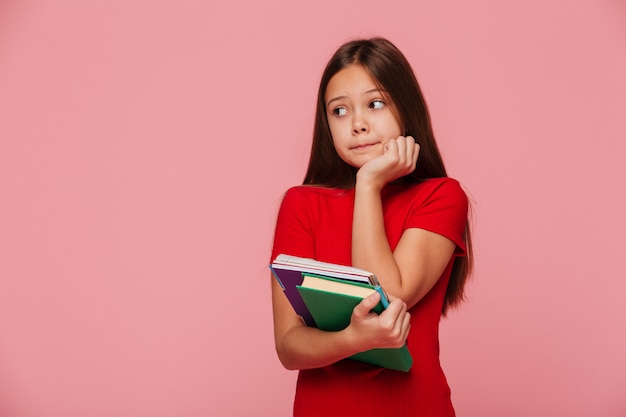 Nadenkend meisje leerling bedrijf boeken en opzij kijken over roze