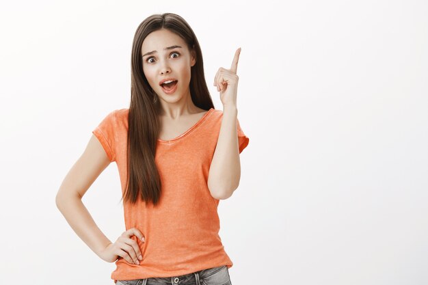 Nadenkend mooi meisje heeft een idee, steekt de vinger op, onthoud iets, bedenk een oplossing