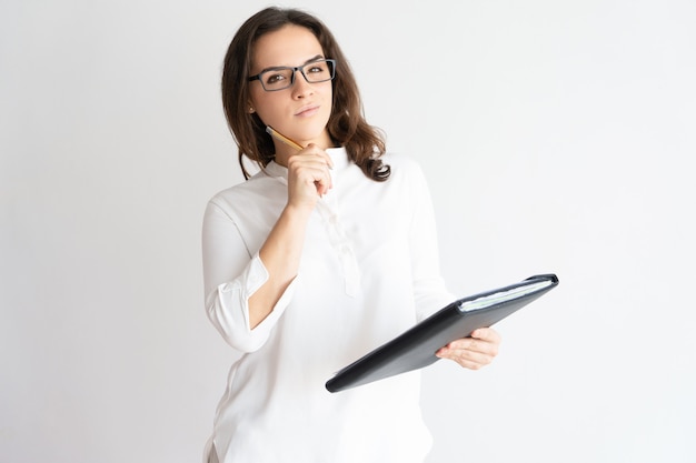 Nadenkend mooie vrouw met bestand, aanraken van gezicht met pen en kijken naar de camera.