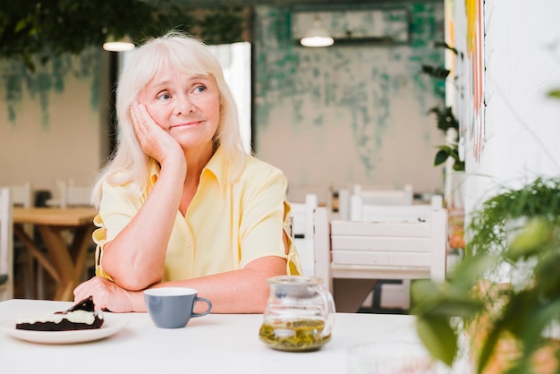 Nadenkend oudere vrouw zitten aan tafel in café