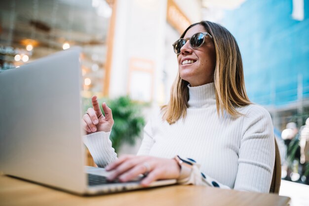 Nadenkend positieve jonge vrouw met behulp van laptop aan tafel in de straat café