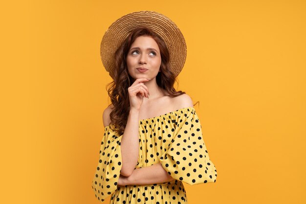Nadenkend roodharige vrouw poseren in gele jurk met mouwen op geel. Zomerstemming.