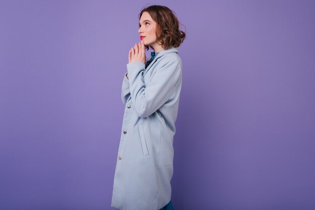 Nadenkend stijlvolle vrouw in lange blauwe jas poseren. Binnenfoto van vrij kortharige dame in herfstkledij.