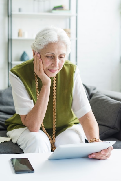 Nadenkende hogere vrouw die digitale tablet bekijkt