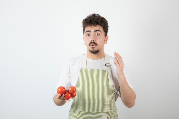 Nadenkende jonge kerel die stapel tomaten houdt en zijn hand opheft.