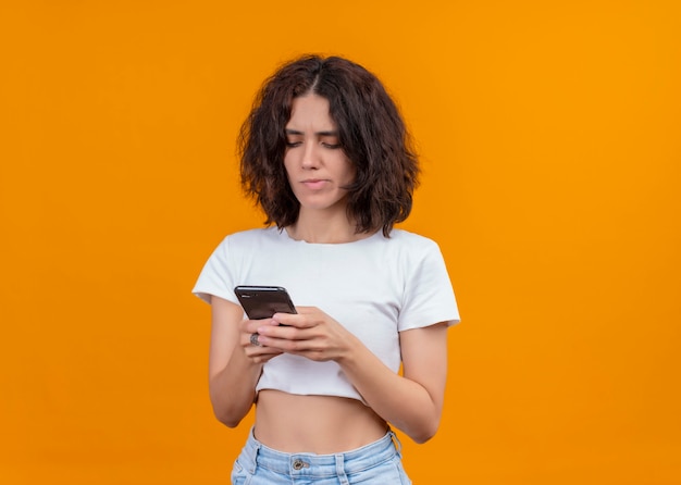 Nadenkende jonge mooie vrouw die mobiele telefoon op geïsoleerde oranje muur met exemplaarruimte houdt