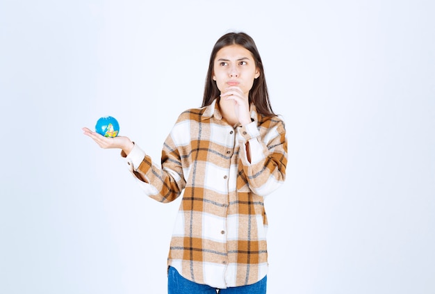 nadenkende jonge vrouw die kleine bol op witte muur bekijkt.