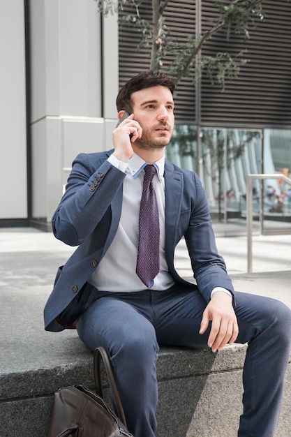 Nadenkende kerel in kostuum die op smartphone spreken