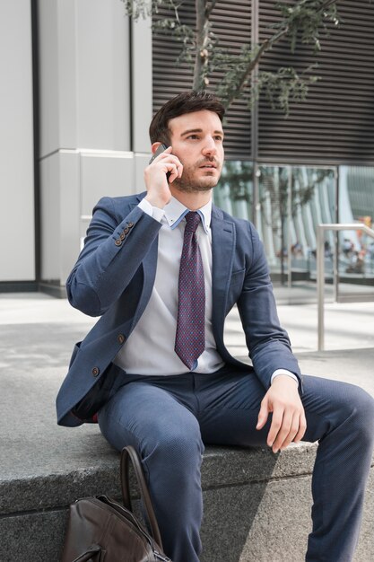 Nadenkende kerel in kostuum die op smartphone spreken