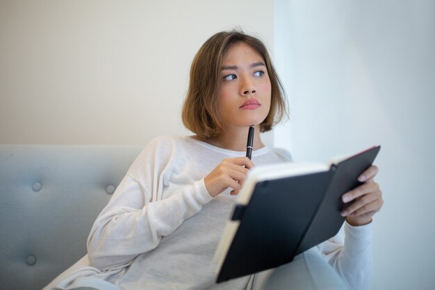 Nadenkende vrij Aziatische vrouw die thuis bestudeert