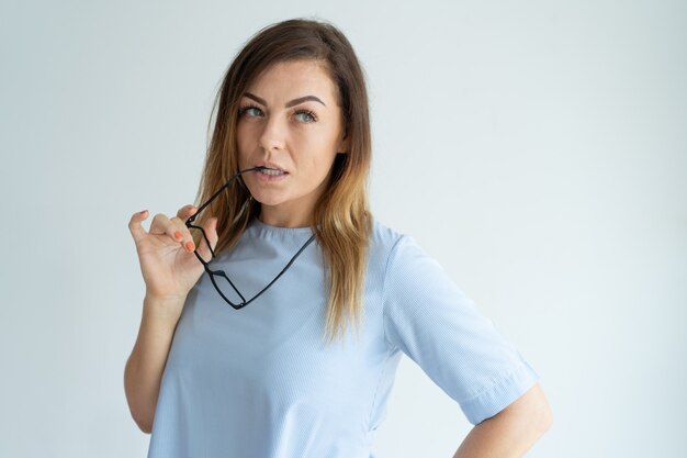 Nadenkende vrouw bijt glazen tempel en wegkijken. Lachende mooie dame denken.