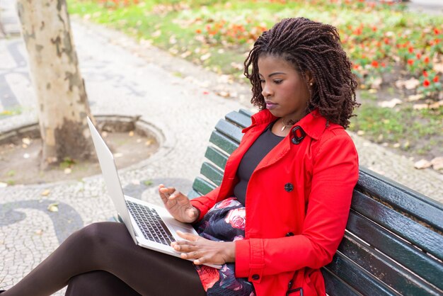 Nadenkende vrouw die op laptop typen terwijl het zitten op bank in park