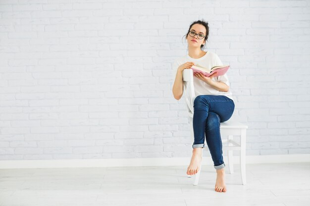 Nadenkende vrouw met boek op stoel