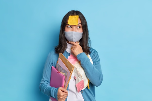 Nadenkende vrouwelijke ondernemer werkt vanuit huis, omdat sociale afstandelijkheid een wegwerpmasker draagt en denkt hoe onderzoekswerk moet worden voorbereid, draagt een casual trui.