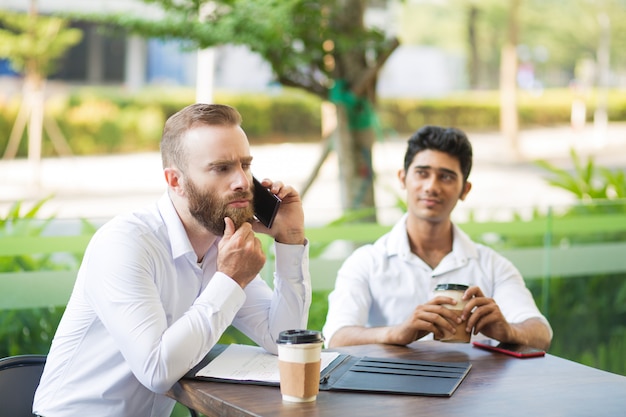 Nadenkende zakenman die baard wrijven terwijl het spreken op telefoon