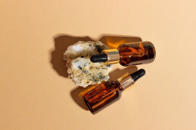 Natuurlijke cosmetica in glazen flessen met een druppelaar staan naast een steen op een beige achtergrond met fel zonlicht. het concept van natuurlijke cosmetica, natuurlijke etherische olie