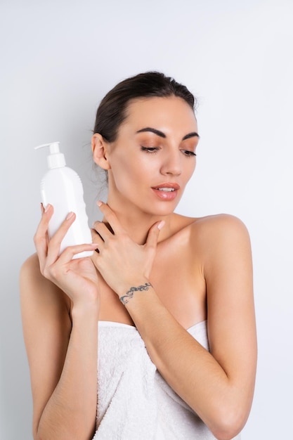 Nauw schoonheidsportret van een topless vrouw met een perfecte huid en natuurlijke make-up die een fles shampoo bodylotion op een witte achtergrond vasthoudt