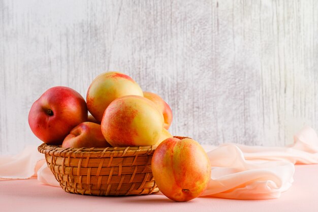 Nectarines in een mand met textiel zijaanzicht op roze en grungy muur