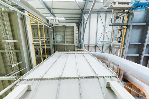 Neerwaarts zicht op moderne operationele fabriek met grijze buizen en ladders zware industrie machines metaalbewerking werkplaatsconcept