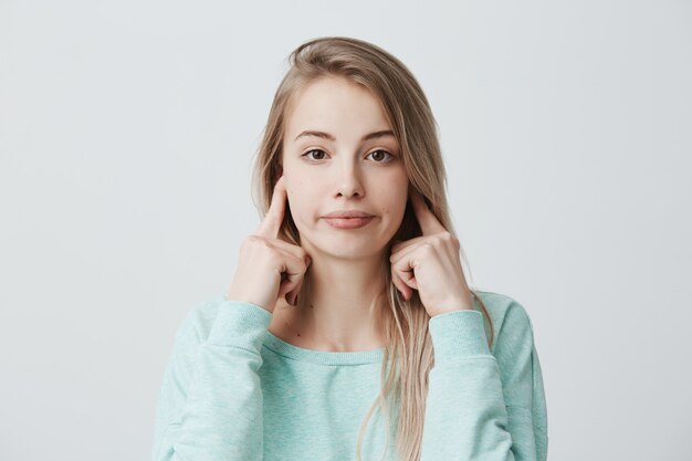 Negatieve menselijke emoties, reactie en houding. Gefrustreerde geïrriteerde vrouw met blond geverfd haar dat oren met vingers verstopt, zich geïrriteerd voelt met hard irritant geluid, zich niet kan concentreren op haar werk