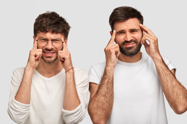 Negatieve menselijke gezichtsuitdrukkingen en emoties. Ontevreden mannen houden hun vingers op de slapen, fronsen hun wenkbrauwen in ontevredenheid, hebben hoofdpijn, dragen vrijetijdskleding