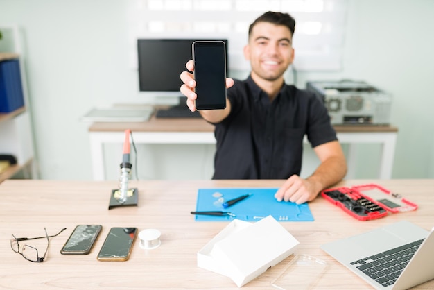 Gratis foto net als nieuw. gelukkige jonge man met een vaste smartphone. glimlachende technicus die het gebroken scherm van een smartphone repareert