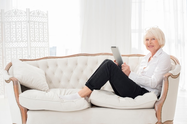 Nette oude vrouw zittend op de Bank met een tablet