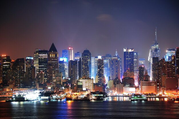 New York City Manhattan midtown skyline 's nachts met wolkenkrabbers verlicht over Hudson River met reflecties.