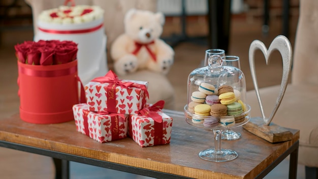 Niemand in de ruimte versierd met bloemenboeket en cadeautjes, zoete macarons en romantische cadeaus op tafel. Lege ruimte met Valentijnsdagverrassing en rode rozen om liefdesvakantie te vieren.