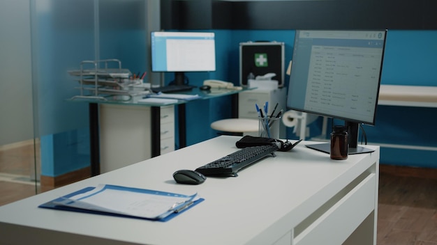 Niemand in kast met medische apparatuur voor controlebezoek en onderzoek. Close up van bureau met computer, documenten en hulpmiddelen voor overleg in lege dokterspraktijk op faciliteit.