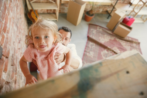 Gratis foto nieuw leven. jonge vader en zijn dochter verhuisden naar een nieuw huis of appartement. zie er gelukkig en zelfverzekerd uit